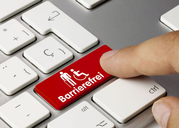 Ein Finger drückt auf eine rote Tastenkappe mit dem Wort "Barrierefrei" und einem Rollstuhl-Piktogramm.